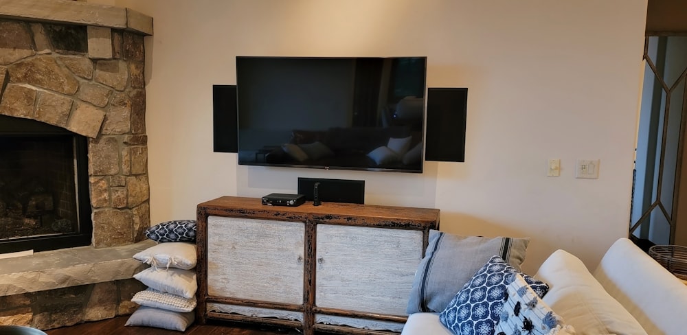 Wall-mounted TV with wall-mounted soundbar and surround speakers beside a stone fireplace